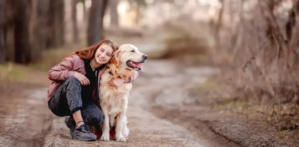 Woman hugging Golden Retriever on forest path.